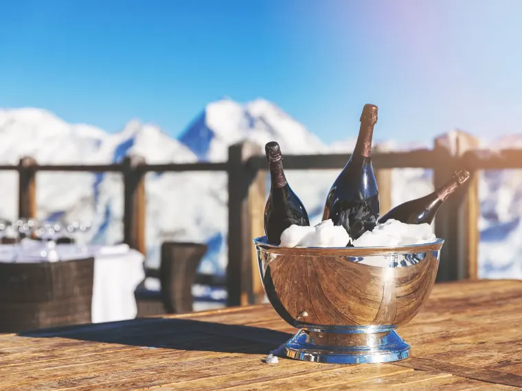 Champagner im Eiskübel auf der Sonnenterrasse vor verschneiten Bergen